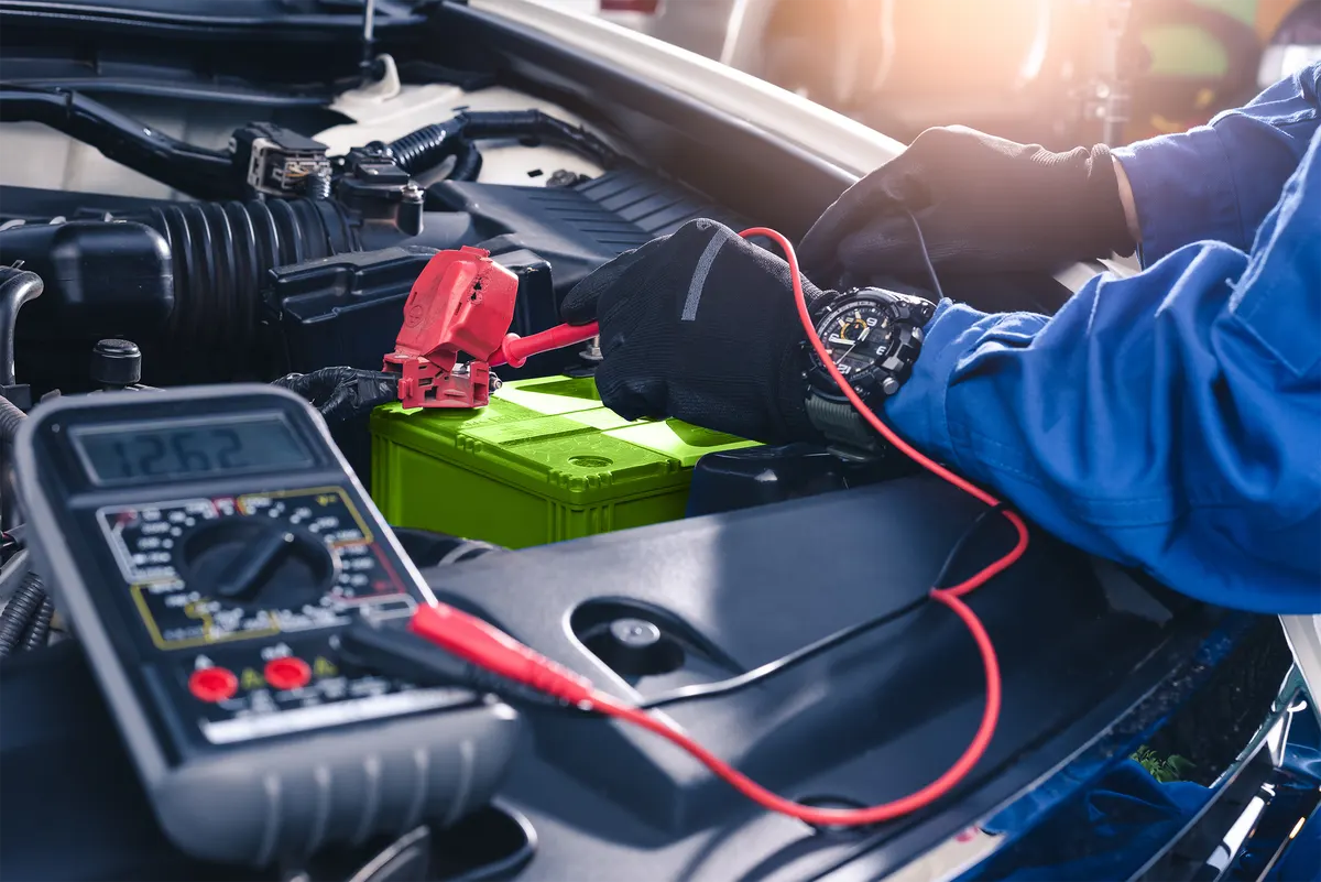 Technician testing a car battery with a multimeter under the bonnet